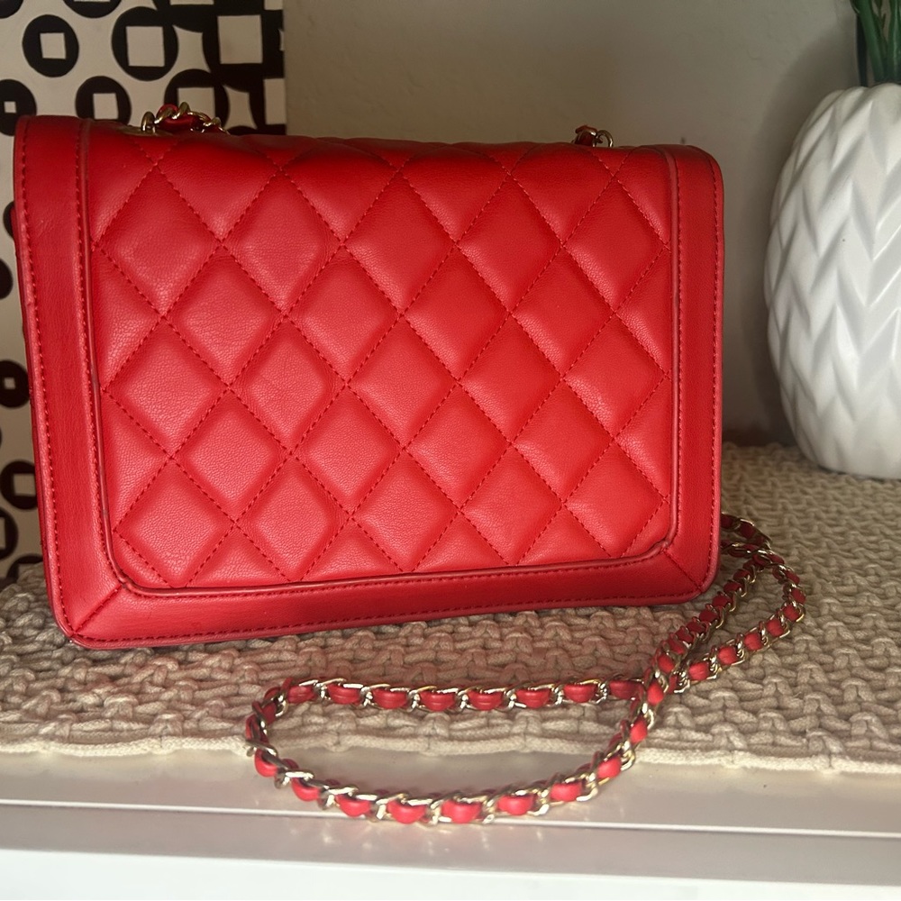 A red, pleated shoulder bag with a gold chain